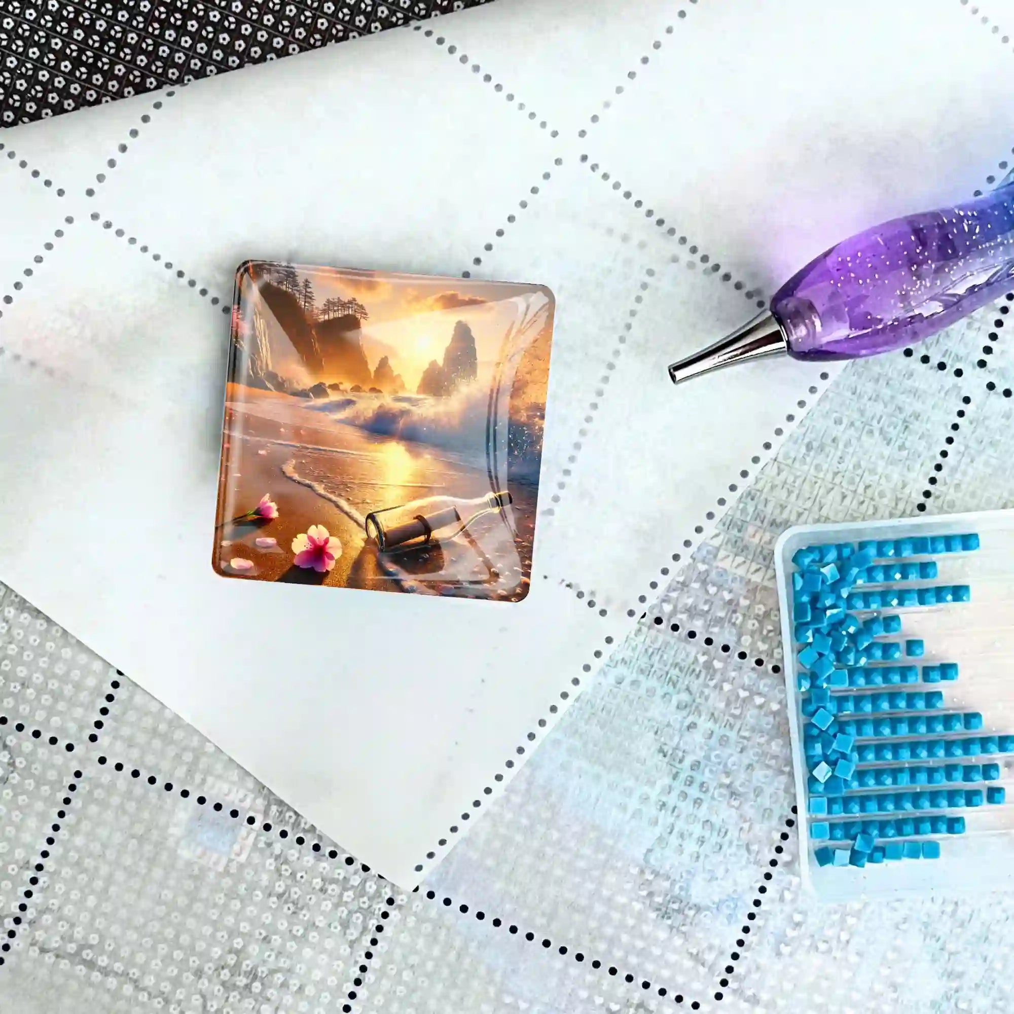 Quadratischer Diamond Painting Cover Minder mit Meeresmotiv auf einer Leinwand mit Stift und blauen Diamanten.