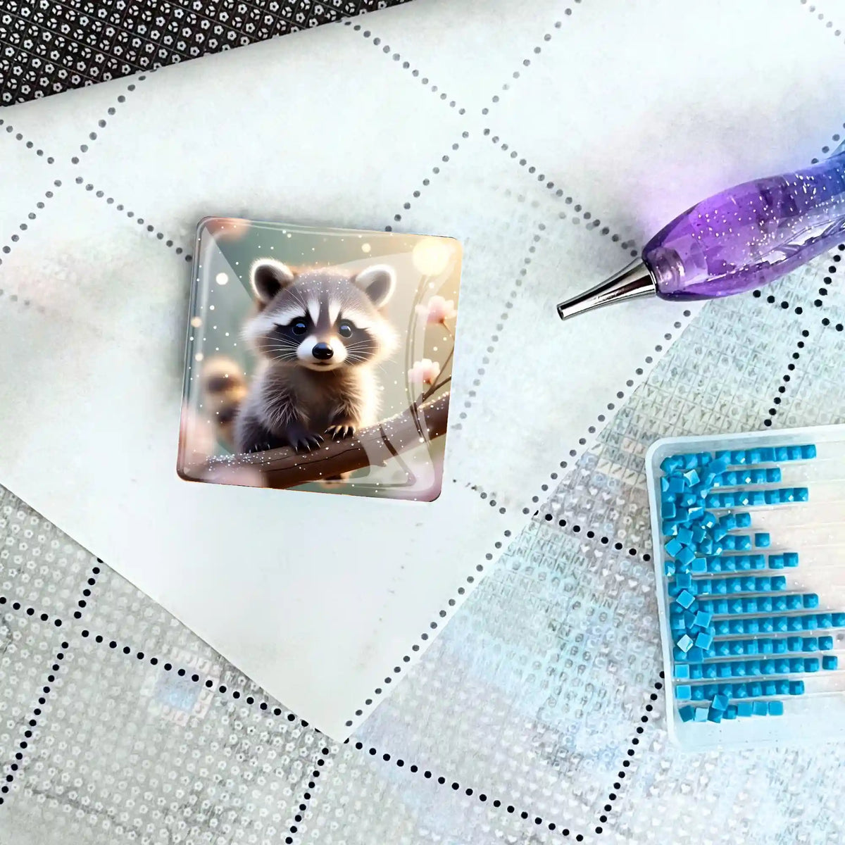 Quadratischer Diamond Painting Cover Minder Waschbär Klettermax auf einer Leinwand mit Applikator und blauen Steinchen